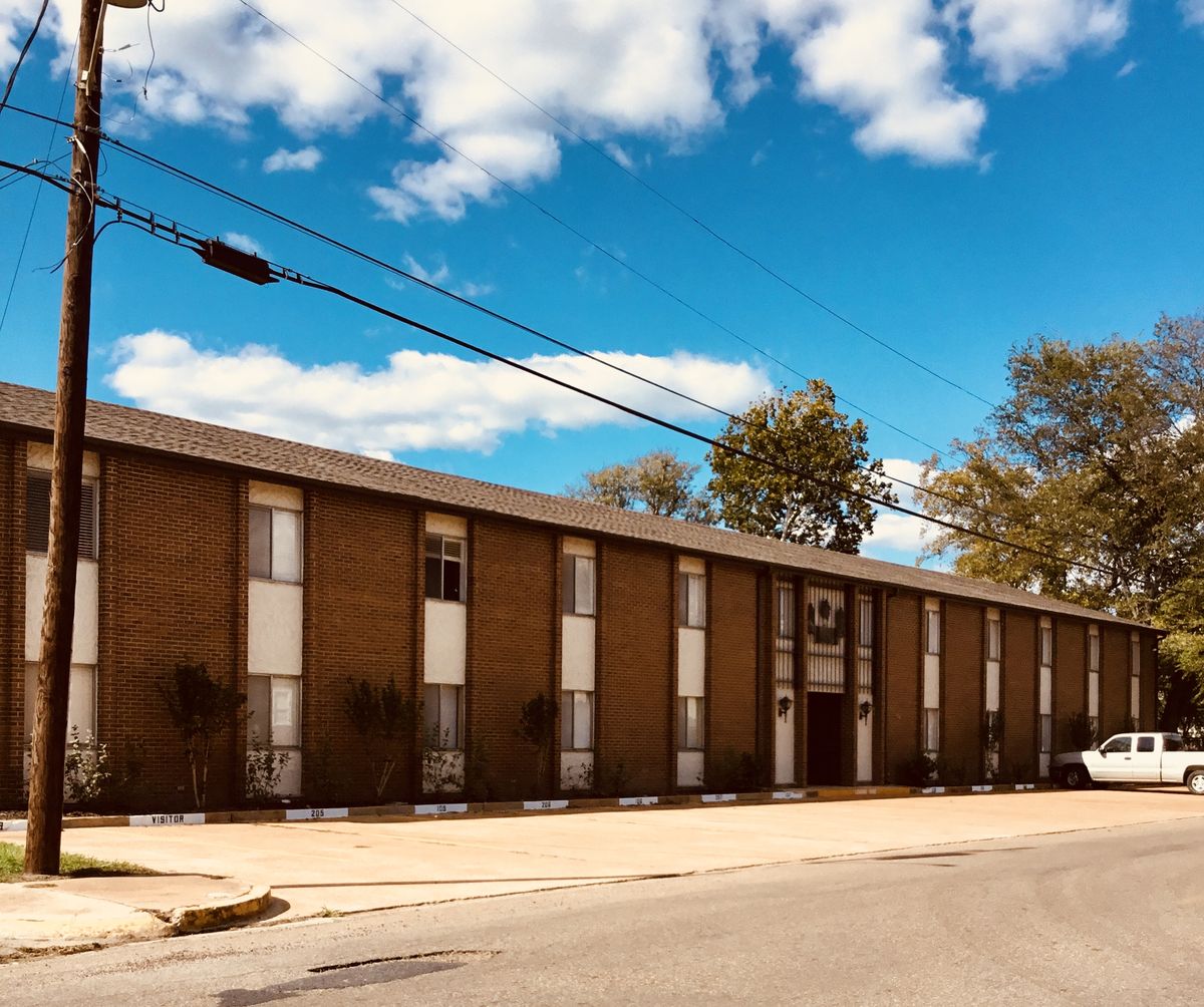 Wide street view of the long two-story brick Ellis Arms building under a blue sky