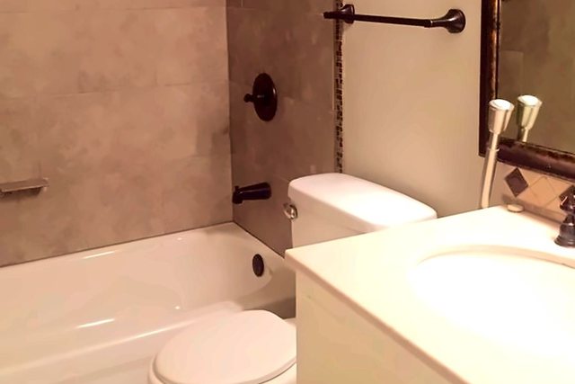 Bathroom in Unit 206 with a tiled tub surround, dark fixtures, and a white vanity