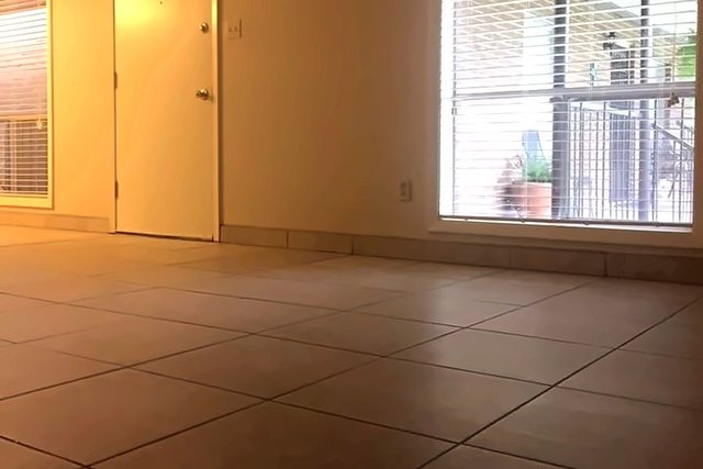 Living room in Unit 206 with light tile flooring, a large window with blinds, and the entry door
