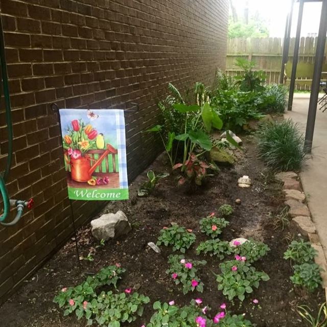 Flower bed with pink flowers and a Welcome garden flag along a brick wall