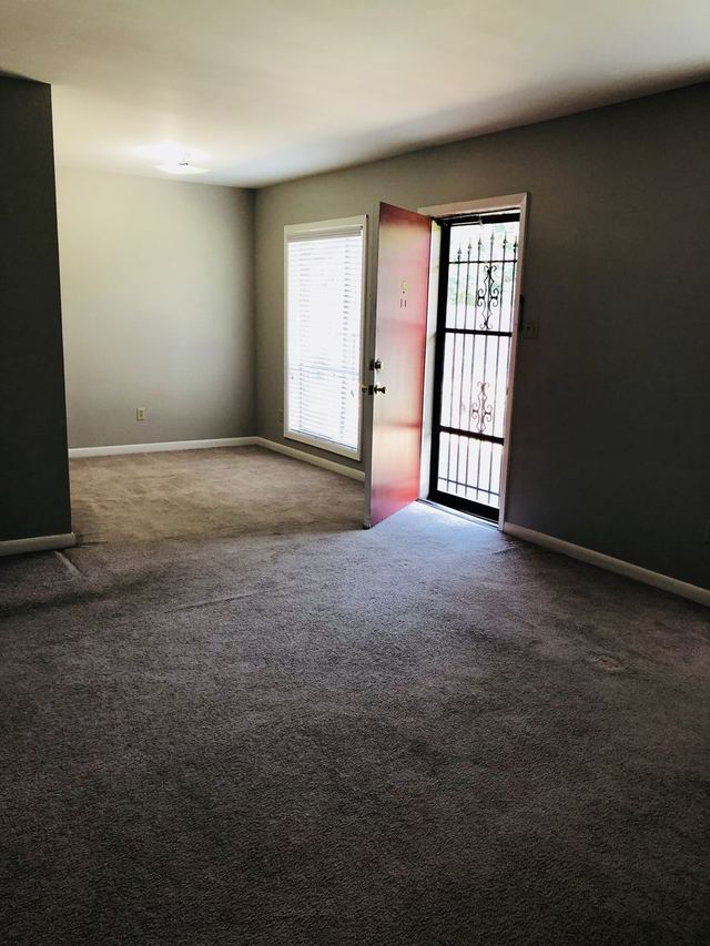 Bright living room in Unit 102 with a red front door open to a decorative iron security door