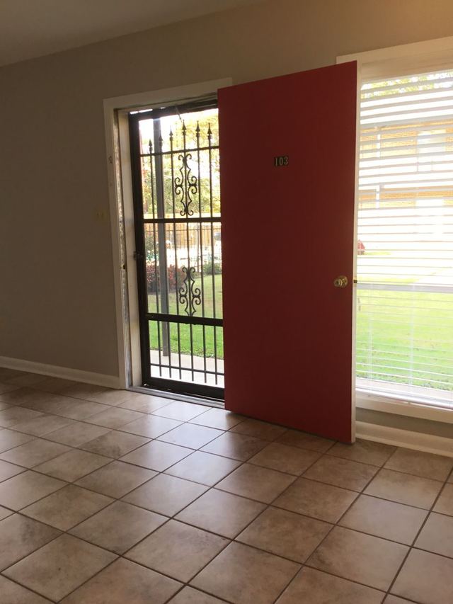 Living room entry in Unit 103 with red door open to a security screen and tile flooring
