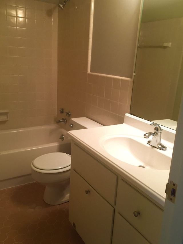 Bathroom in Unit 203 with a white vanity, toilet, and tiled tub surround