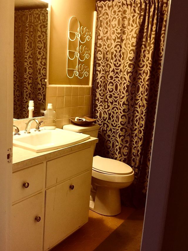 Bathroom in Unit 207 with vanity, toilet, clean wall tile and grout, and patterned shower curtain — furniture and decor not included
