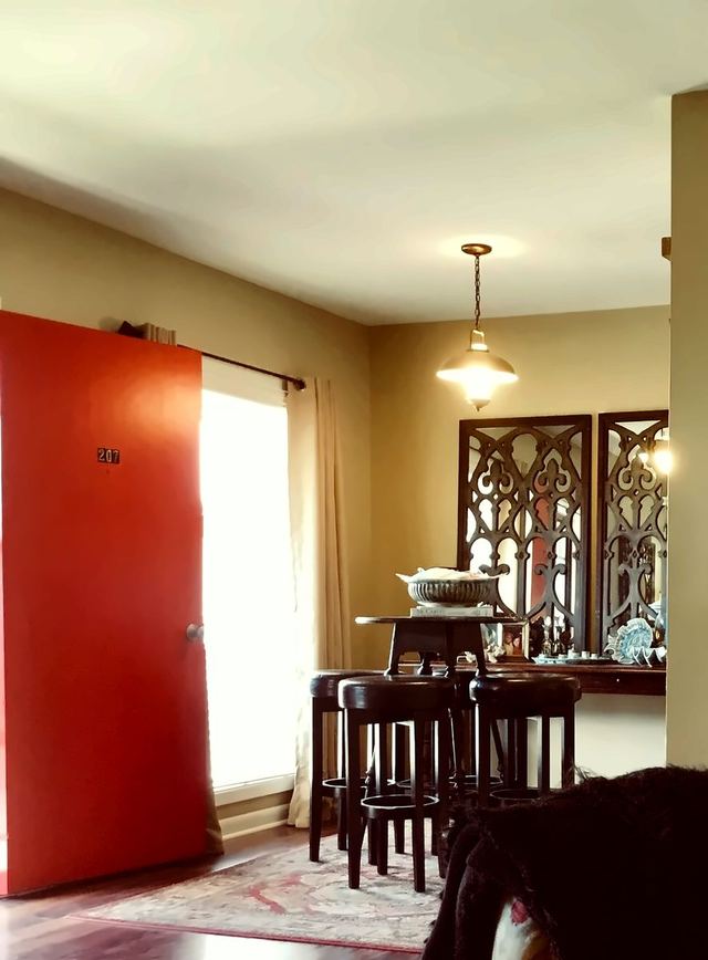 Living and dining area in Unit 207 looking toward the red front door marked 207 and wood-look flooring