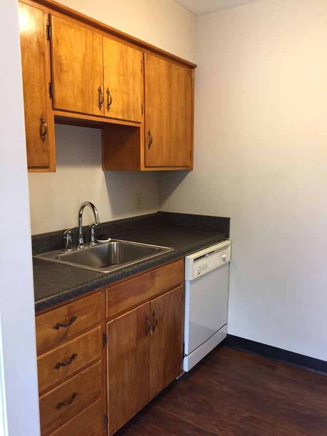 Upgraded unit kitchen with wood cabinets, white dishwasher, and Agreeable Gray walls